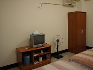 Habitación de hotel con una televisión sobre un soporte de madera, un ventilador, un armario y una cama con ropa de cama a rayas.