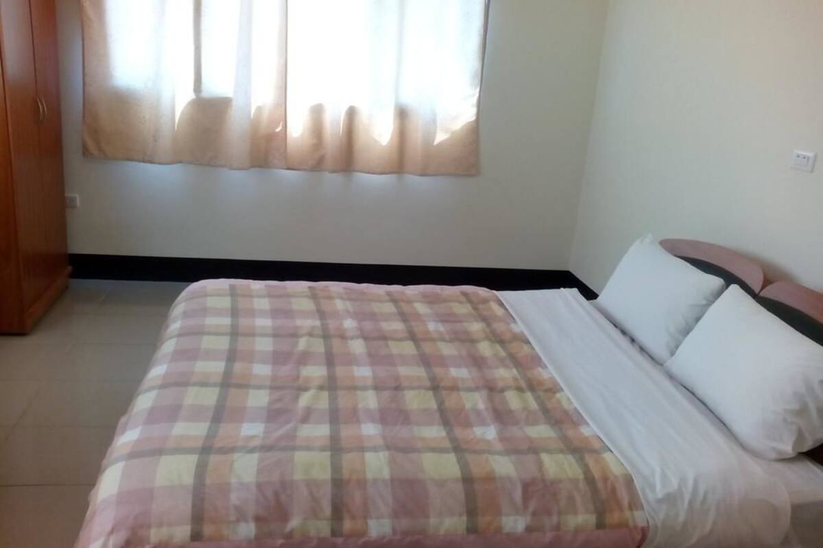 A bedroom with a bed, a window with curtains, and a wall socket.