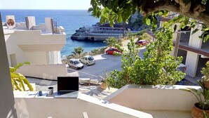A balcony with a laptop, notebook, and pen, overlooking a parking area and a coastal view. - Popis sea view apartments ''Studio Dim'' (Mades, Gazi, Iraklion)
