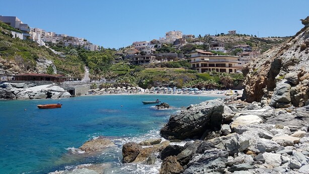A coastal area with rocky terrain, clear blue water, and buildings on a hillside. - Popis sea view apartments ''Studio Dim'' (Mades, Gazi, Iraklion)