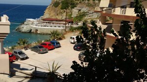 A coastal view with a parking area, a bridge, and buildings with balconies overlooking the sea. - Popis sea view apartments ''Studio Dim'' (Mades, Gazi, Iraklion)