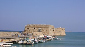 Une structure fortifiée entourée de douves, avec des bateaux amarrés dans l’eau, et un ciel dégagé.