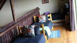 A cozy room with a loft bed, a desk, and a chair. There are wooden beams on the ceiling and a window with curtains. - 24 Bush House (Bela-Bela)
