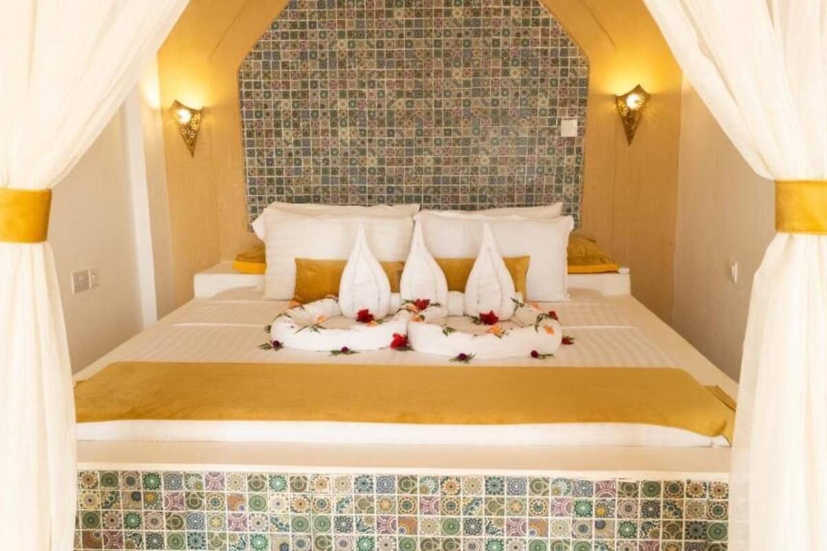 Ein Bett mit weißen Leinentüchern, einem goldfarbenen Kopfteil und einer dekorativen Blumenanordnung.