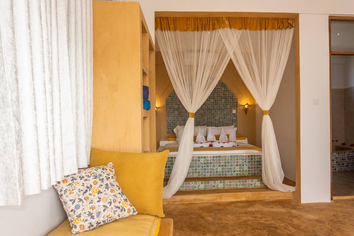 Ein Zimmer mit einem Bett, einem Sofa und einem durch einen Bogen sichtbaren Badezimmer.