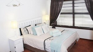 A bedroom with a bed, bedside tables, a lamp, and a window with curtains. - 303 Kusweg (Great Brak River)
