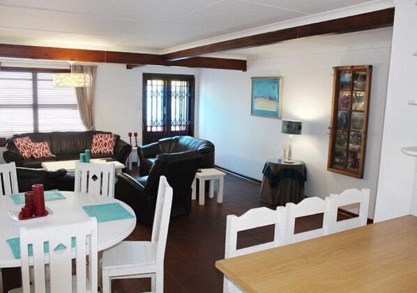 A living room with a sofa, chairs, a dining table, and a small table with a lamp.