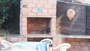 An outdoor brick fireplace with a sign above it, surrounded by stone steps and white plastic chairs. - 303 Kusweg (Great Brak River)