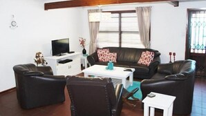 A living room with a sofa, two armchairs, a coffee table, a TV, and a window with curtains. - 303 Kusweg (Great Brak River)