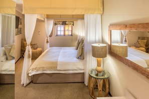 Une chambre à coucher avec un lit, une table de chevet, une lampe, un miroir et une fenêtre avec des rideaux.