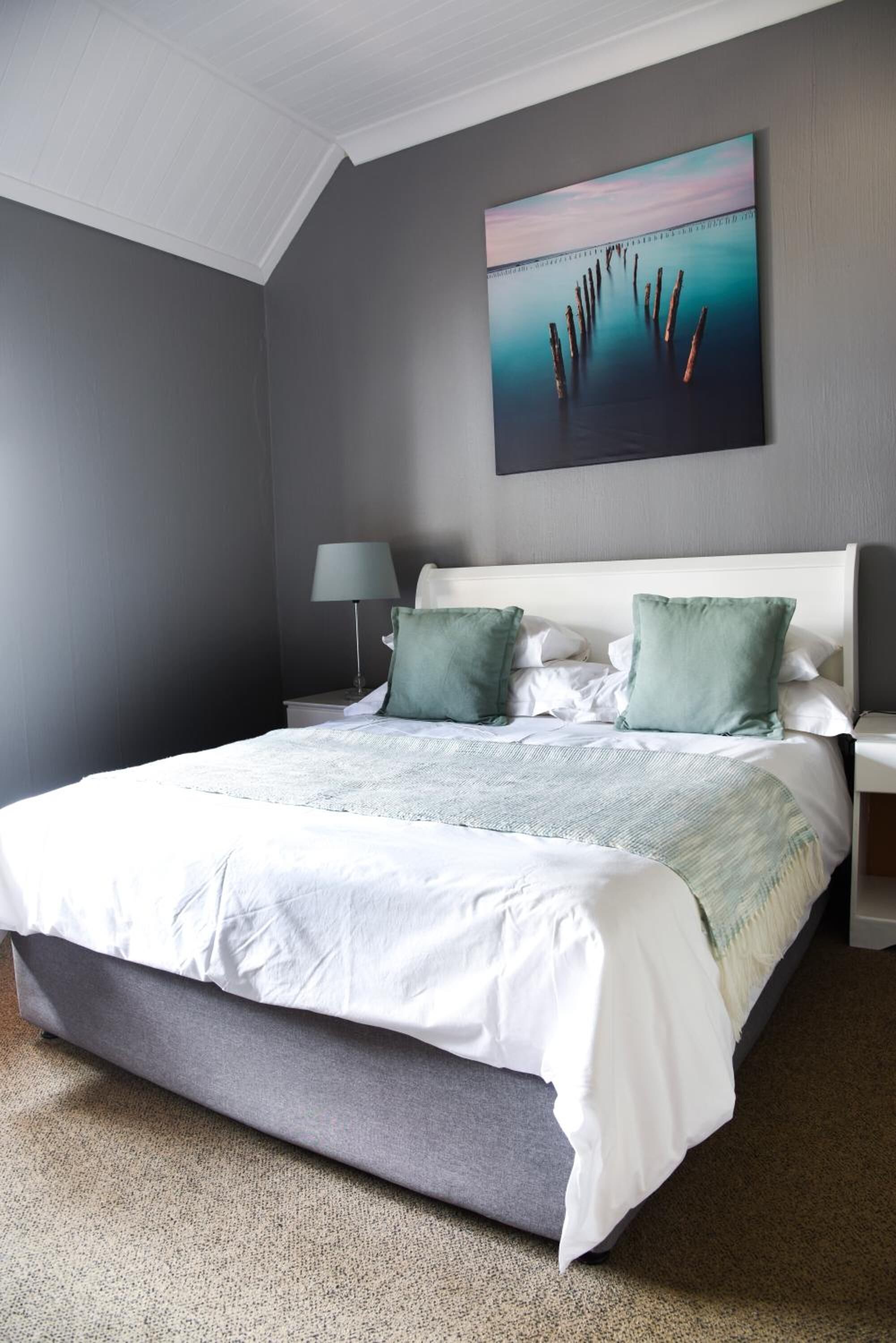 A bedroom with a large bed, a nightstand, a lamp, and a painting on the wall.