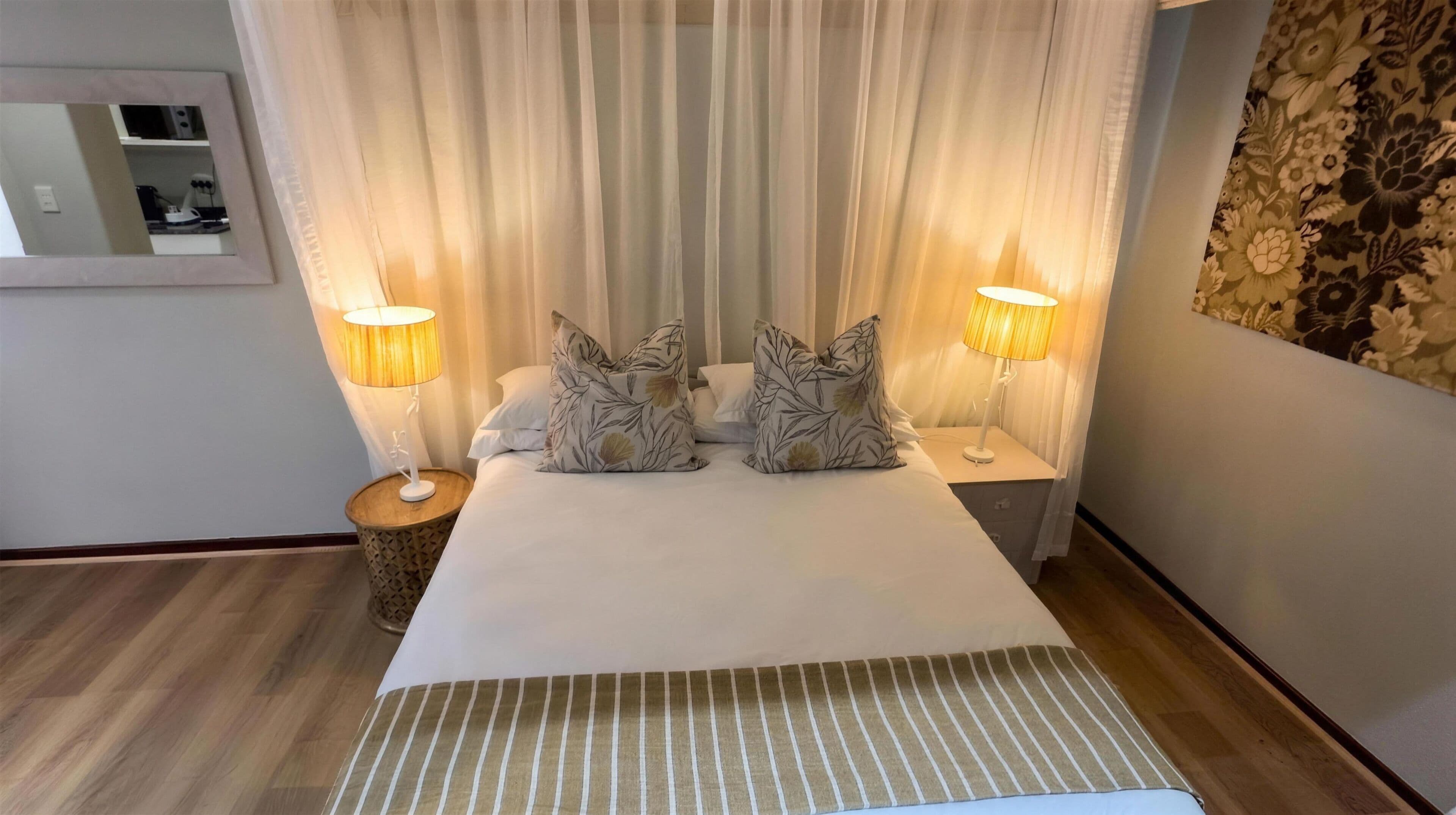 Een hotelkamer met een groot bed, twee bedlampen, een spiegel en een behang met patroon.