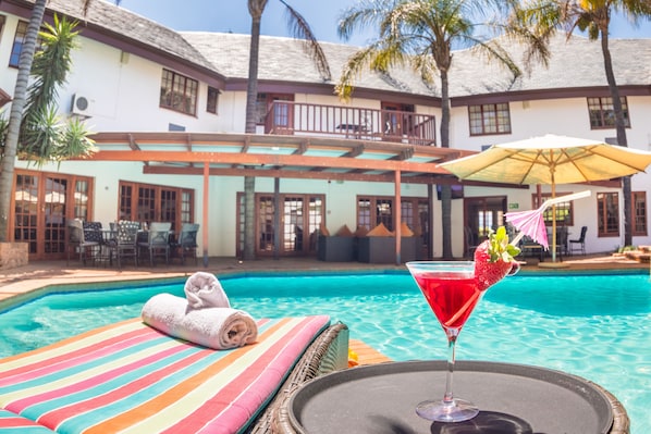 Un espace piscine avec un fauteuil de relaxation, une serviette et un cocktail.