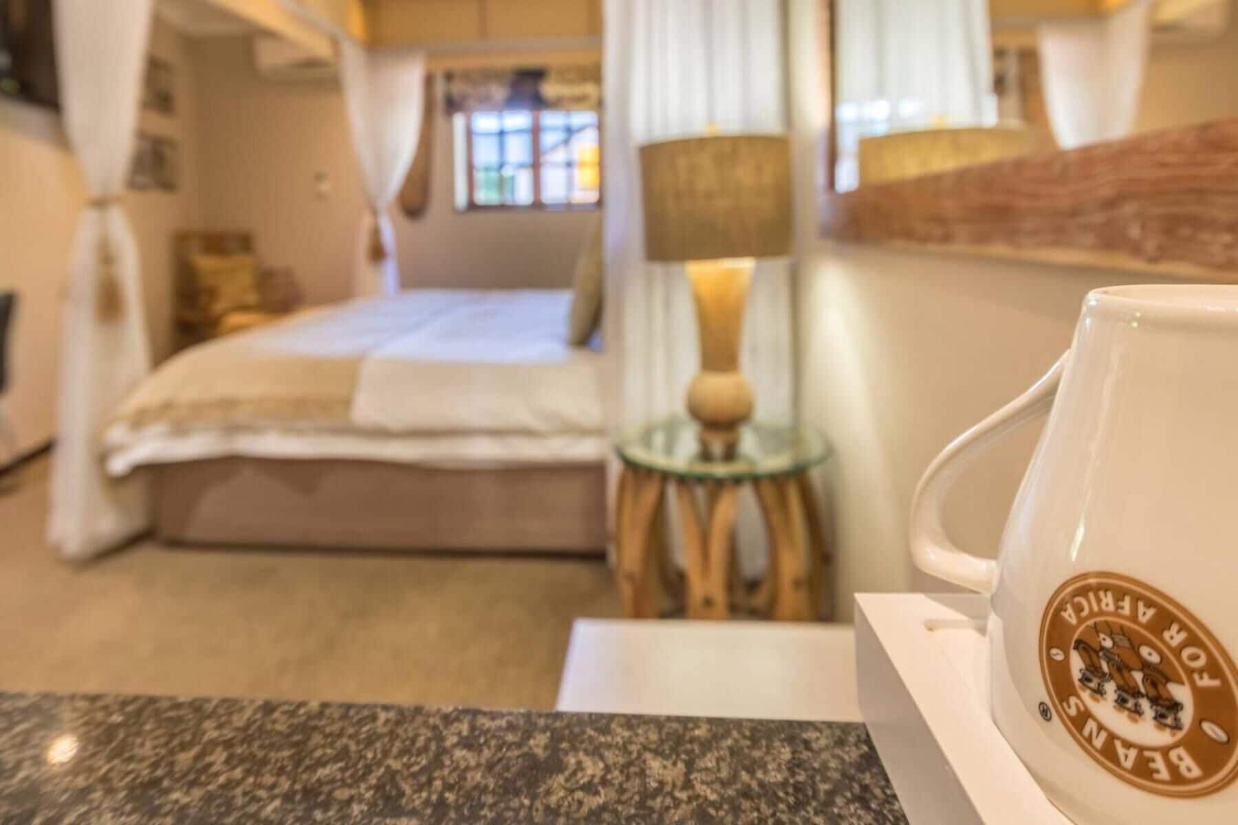 A hotel room with a bed, a small table with a lamp, and a coffee cup on a table.