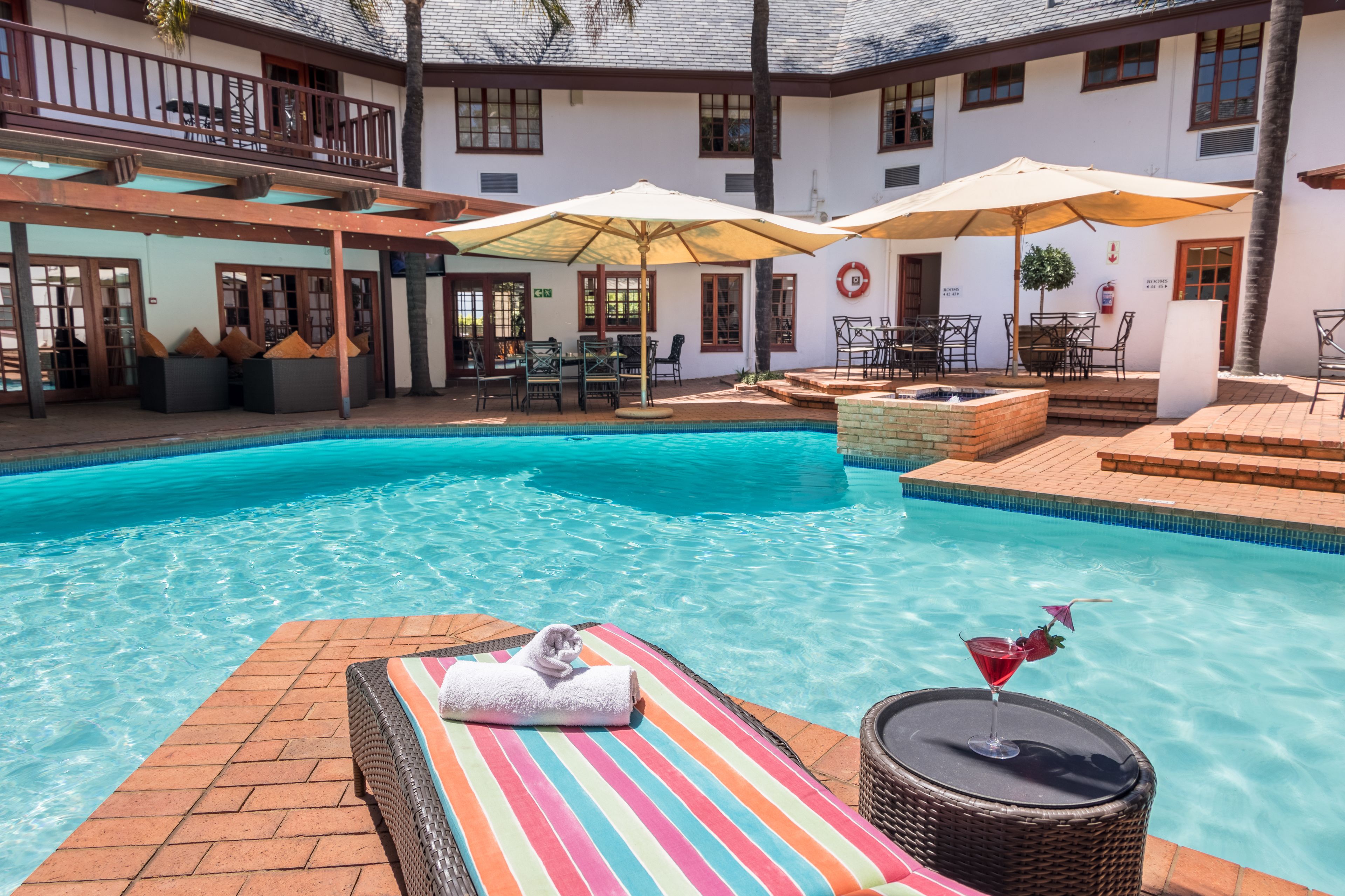 A swimming pool with lounge chairs and umbrellas, a covered patio area, and a brick pathway.