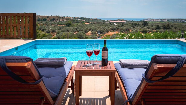 Escena junto a la piscina con dos sillones de descanso, una mesa con una botella de vino y dos copas, y vistas al paisaje.