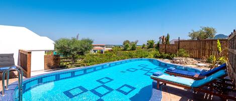A clear blue swimming pool with a tiled deck, surrounded by wooden fences and lounge chairs.