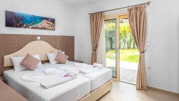 Une chambre d’hôtel avec deux lits, une grande fenêtre avec des rideaux, un tableau représentant une plage et une vue sur la verdure à l’extérieur.