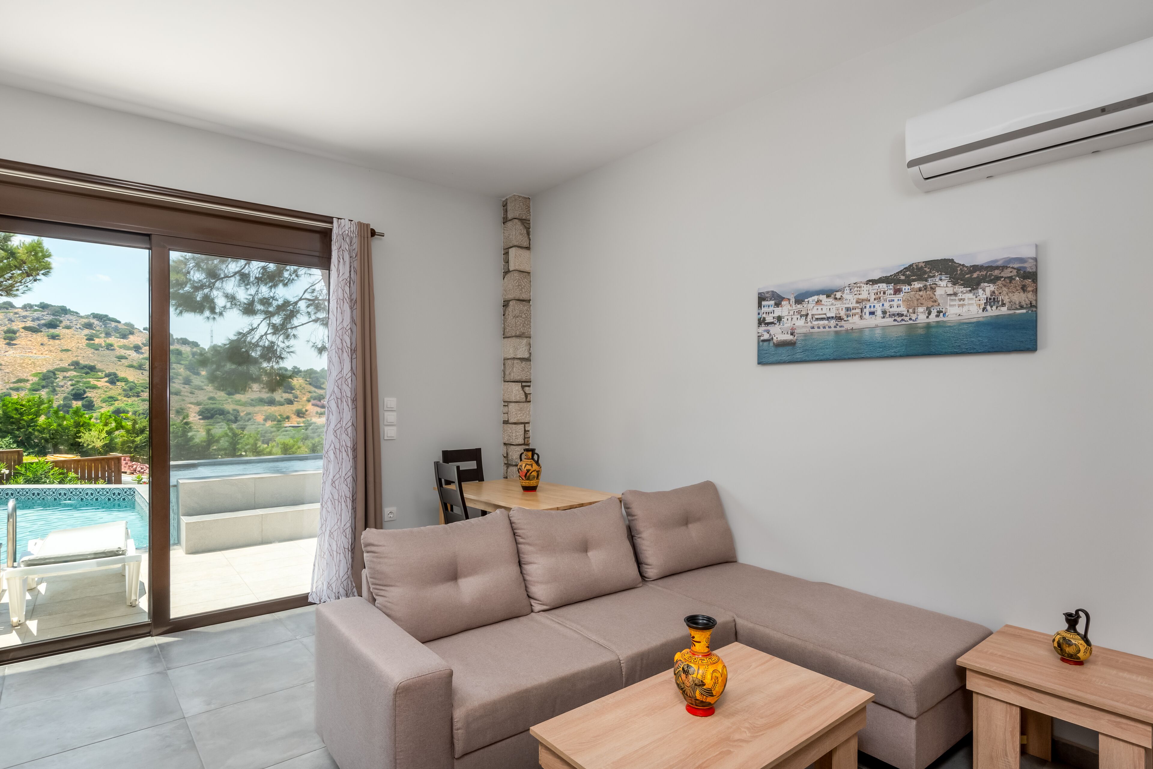 Un salón moderno con un sofá beige, una mesa de centro de madera y vistas a una piscina y una colina.