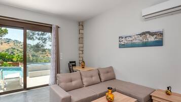 Un salón moderno con un sofá beige, una mesa de centro de madera y vistas a una piscina y una colina.