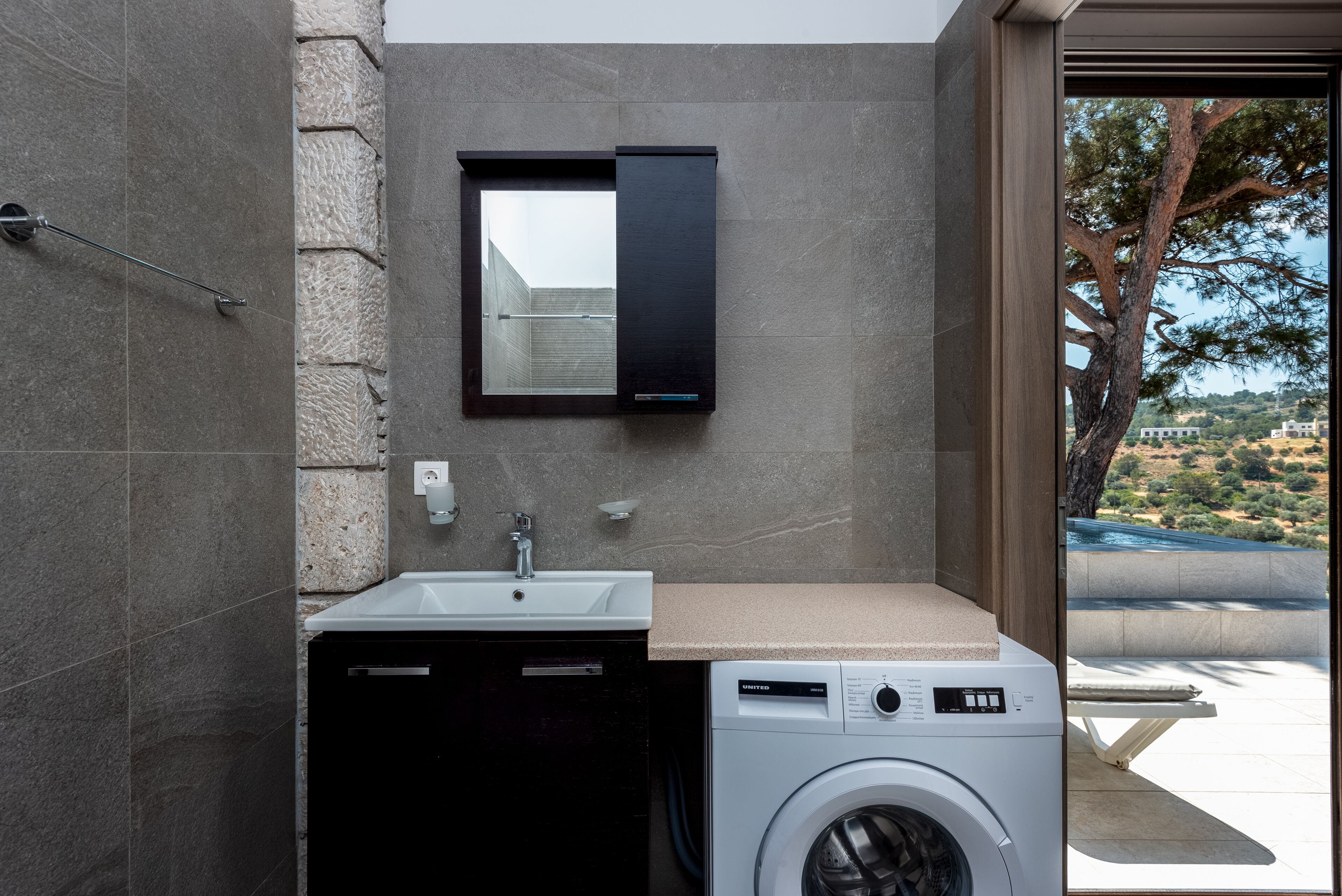 A modern bathroom with a washing machine, a sink, and a mirror.