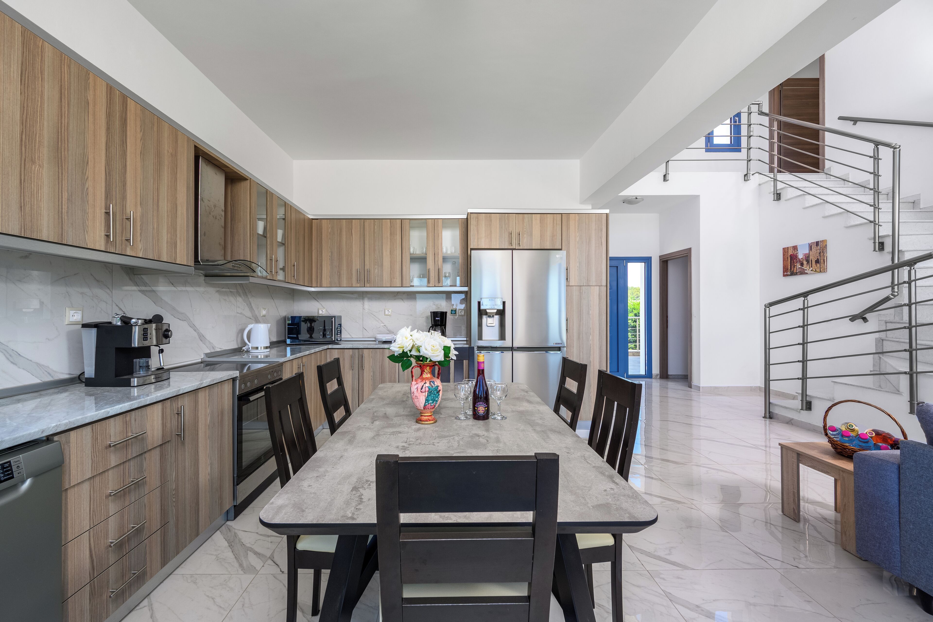 Una cocina moderna con armarios de madera, encimera de mármol y comedor con mesa y sillas.
