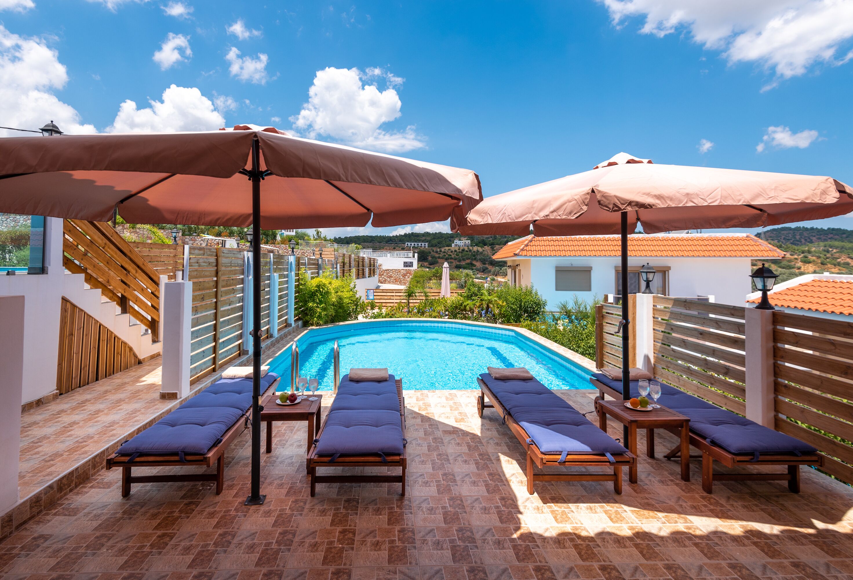 A rooftop pool area with sun loungers and umbrellas, a clear view of the pool, and a wooden deck.