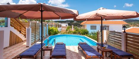 A rooftop pool area with sun loungers and umbrellas, a clear view of the pool, and a wooden deck.