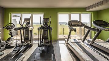 Un gimnasio con diversas máquinas de cardio, ventanas amplias y vistas al exterior.