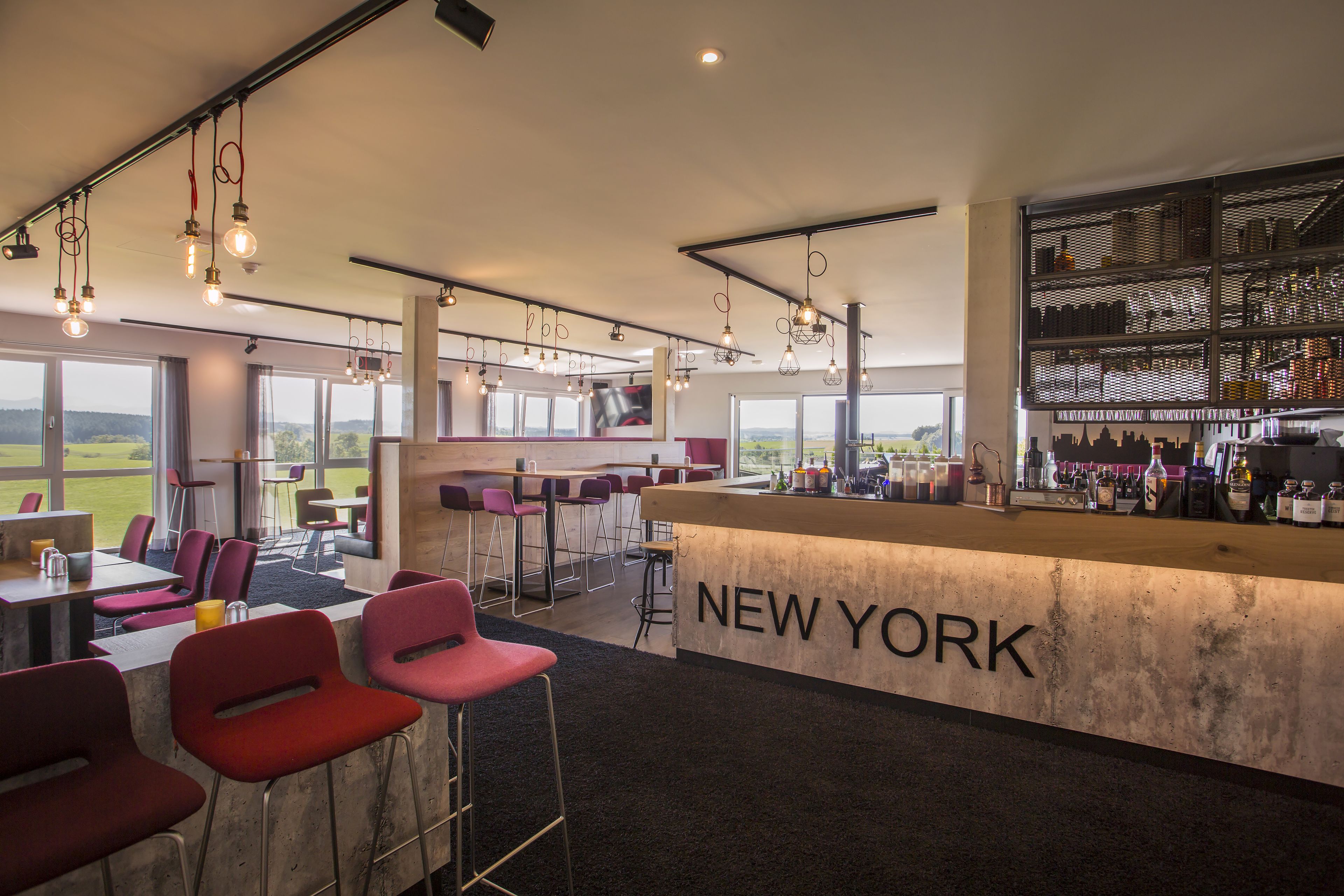 A modern bar area with a 'NEW YORK' sign, bar stools, and a view of the outdoors.