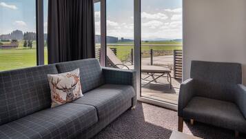 A modern living room with a grey sofa, a matching armchair, and a large window offering a view of a green field and distant hills.
