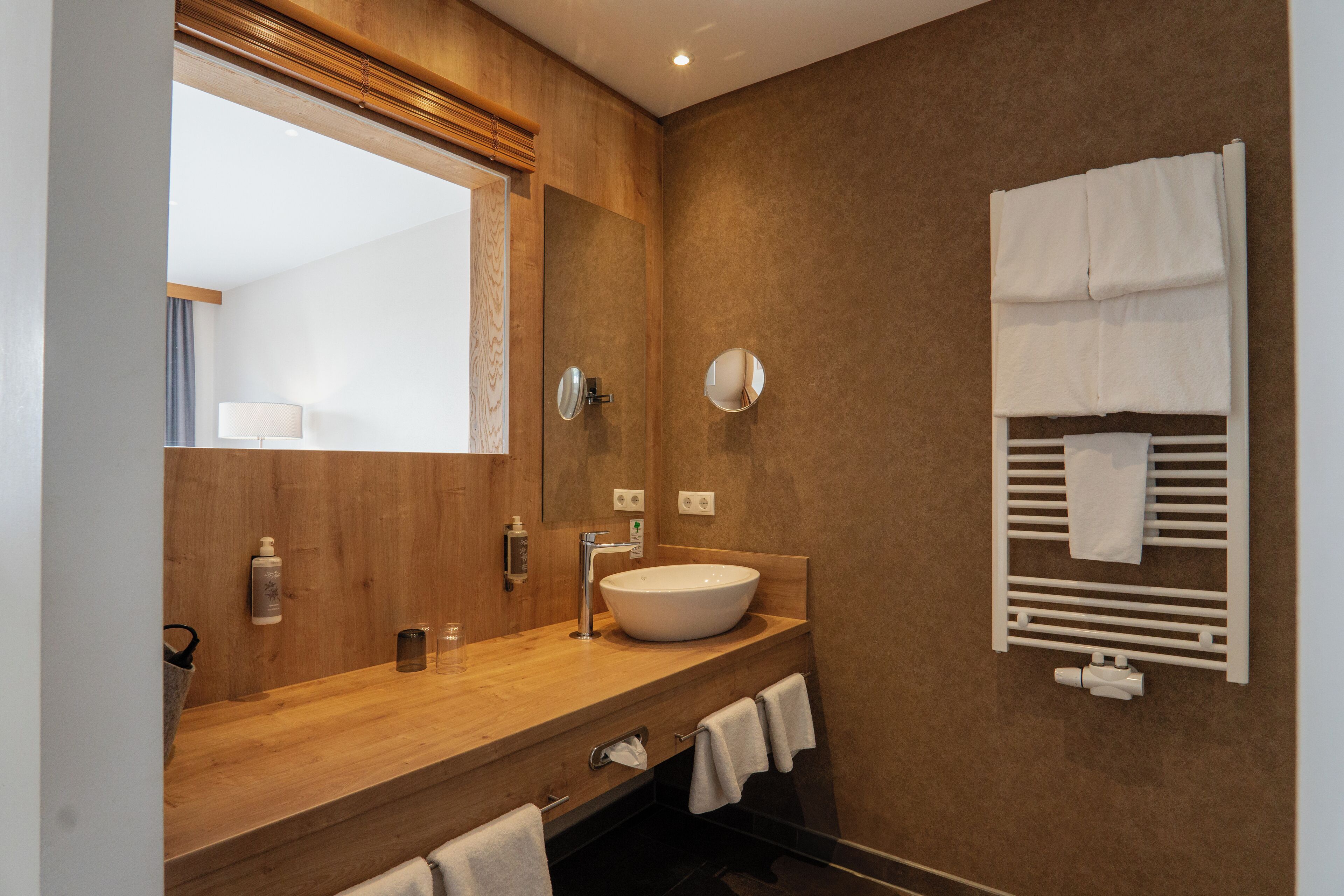 Une salle de bain moderne avec un meuble-lavabo en bois, un grand miroir, un porte-serviettes intégré et un lavabo blanc.