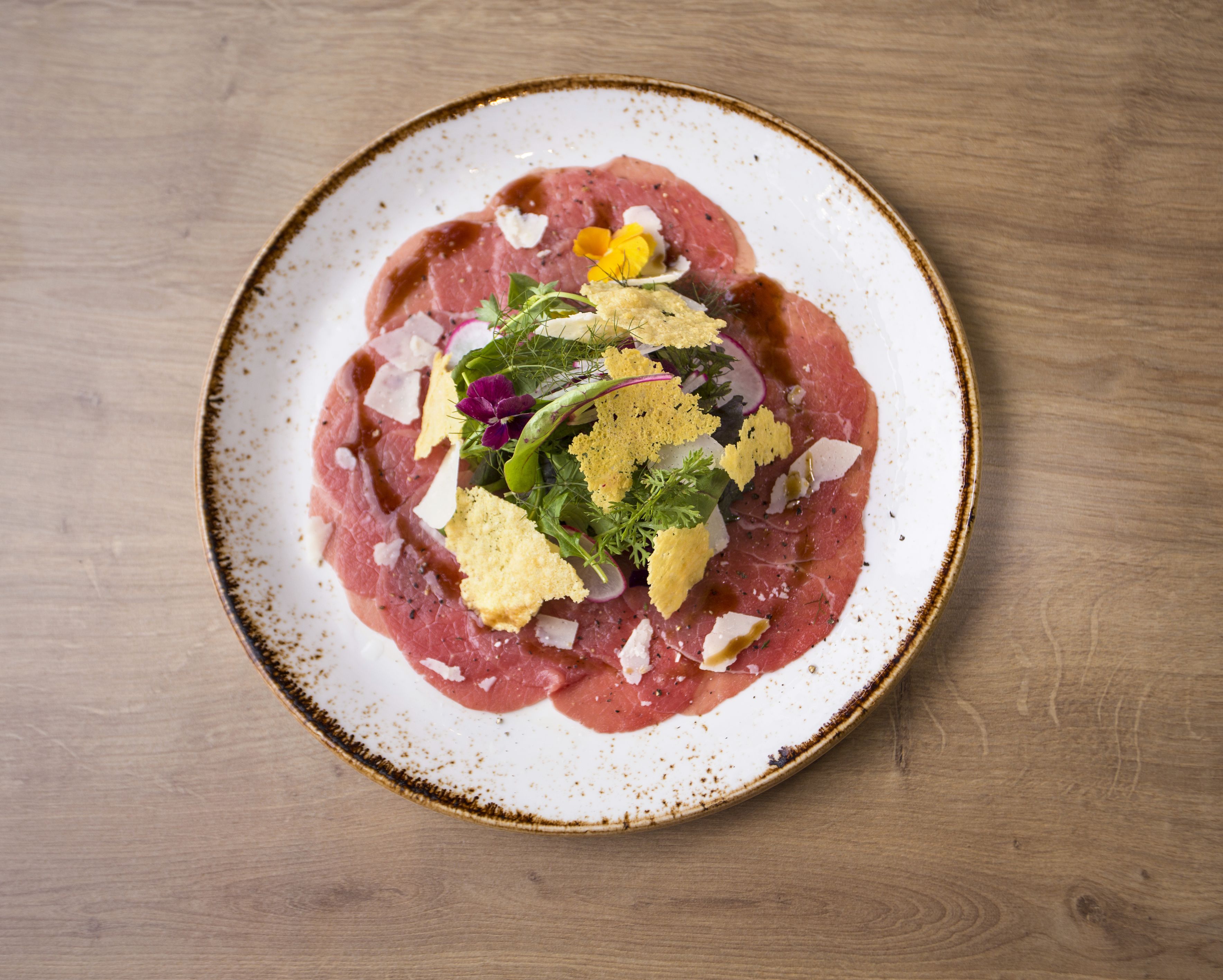 A plate of raw meat with garnishes on a ceramic plate.