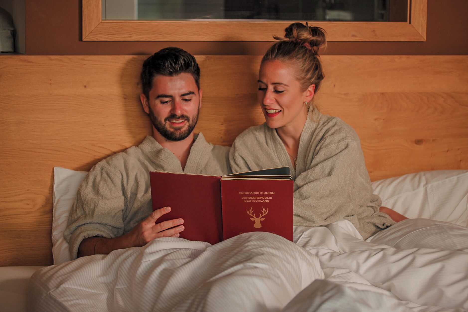 Deux personnes en peignoir sont assises sur un lit, et un livre intitulé « UNION EUROPÉENNE, RÉPUBLIQUE FÉDÉRALE D’ALLEMAGNE » se trouve à proximité.