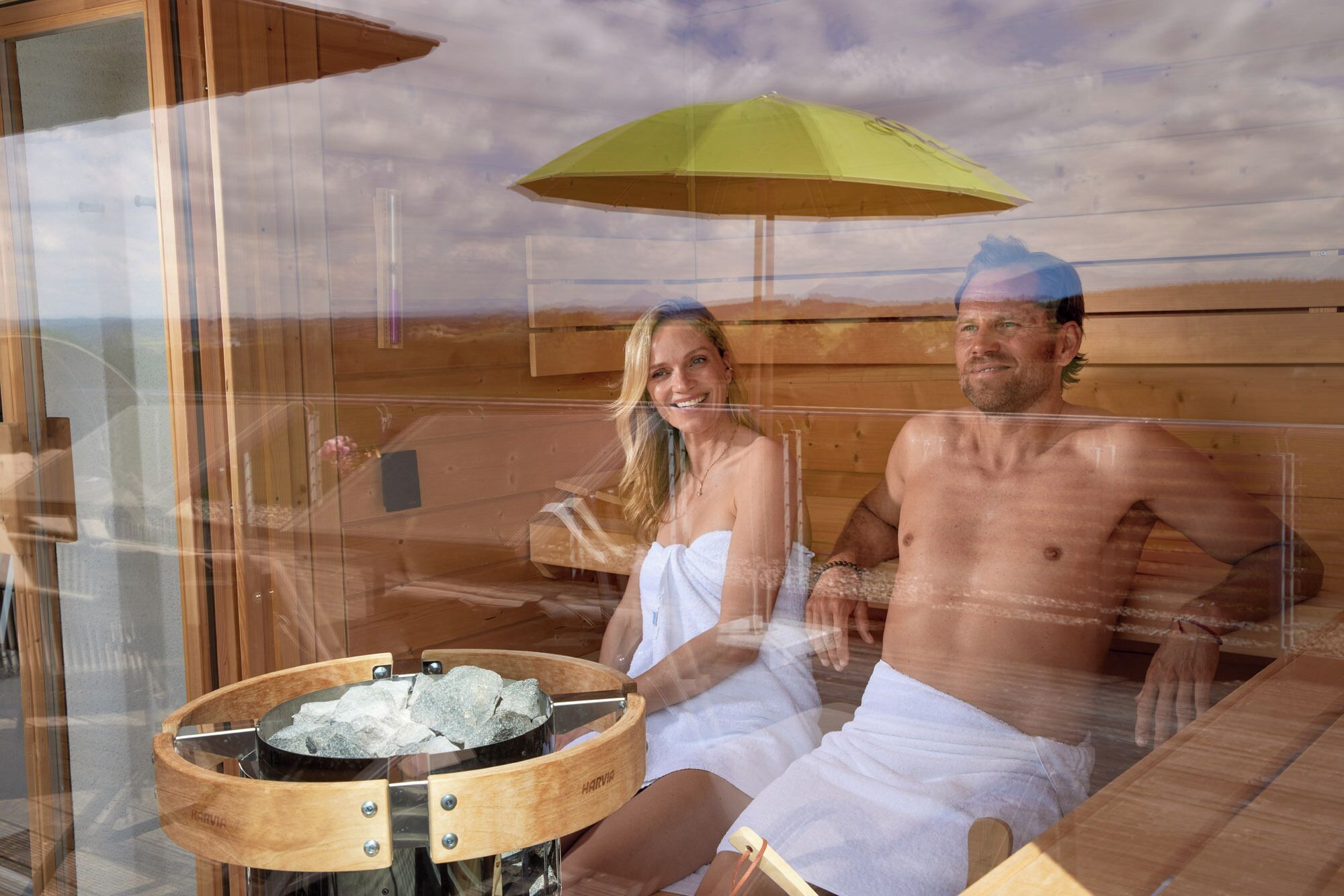 A sauna room with wooden walls, a glass door, and a wooden table with rocks.