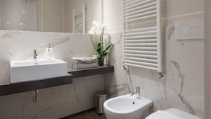 Une salle de bain moderne avec un lavabo en marbre, un bidet et des toilettes, un porte-serviettes et une orchidée en pot.