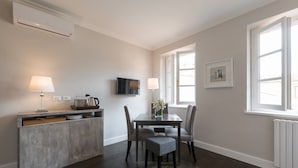 Une cuisine moderne dotée d’un îlot central intégré, d’une table à manger avec des chaises, d’un téléviseur fixé au mur et d’une fenêtre laissant entrer la lumière naturelle.