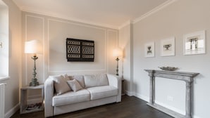 Un salon avec un canapé de couleur claire, deux tables d’appoint avec des lampes, une cheminée et des œuvres d’art murales.