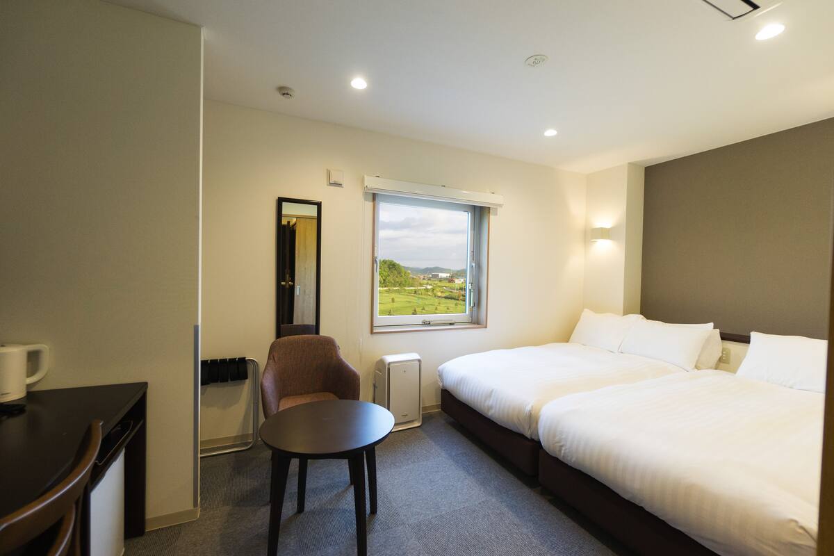 A hotel room with a bed, a chair, a table, and a window with a view of the outdoors.
