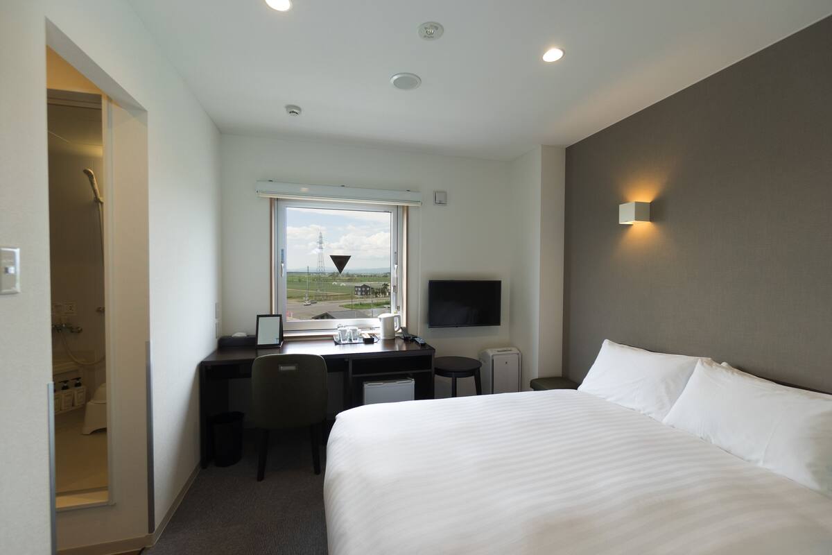 A hotel room with a bed, desk, chair, and a TV mounted on the wall.