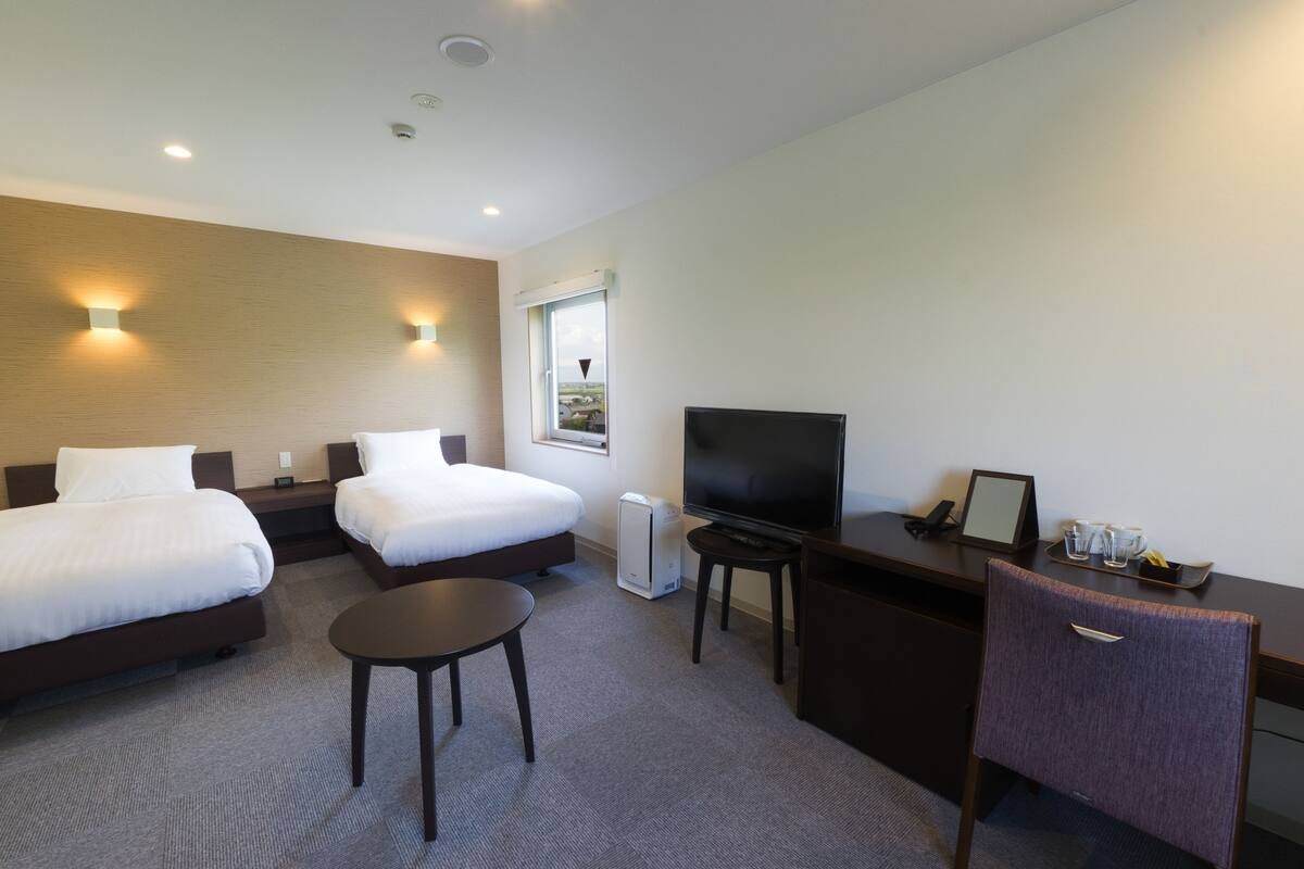 A hotel room with two beds, a desk with a TV, a small table, and a chair.