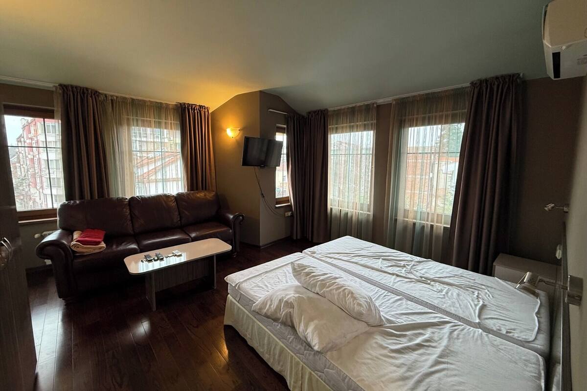Quarto de hotel com cama, sofá, mesa pequena e televisão.