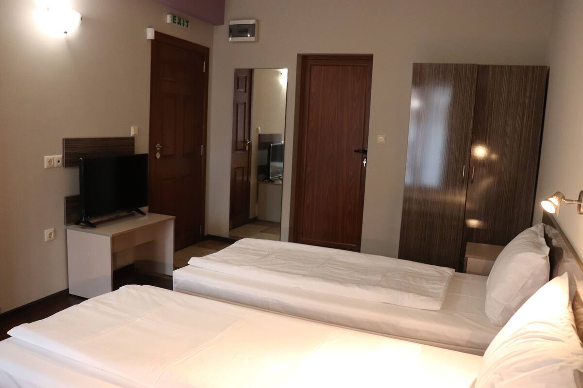 Quarto de hotel com cama, televisão, escrivaninha e guarda-roupa.