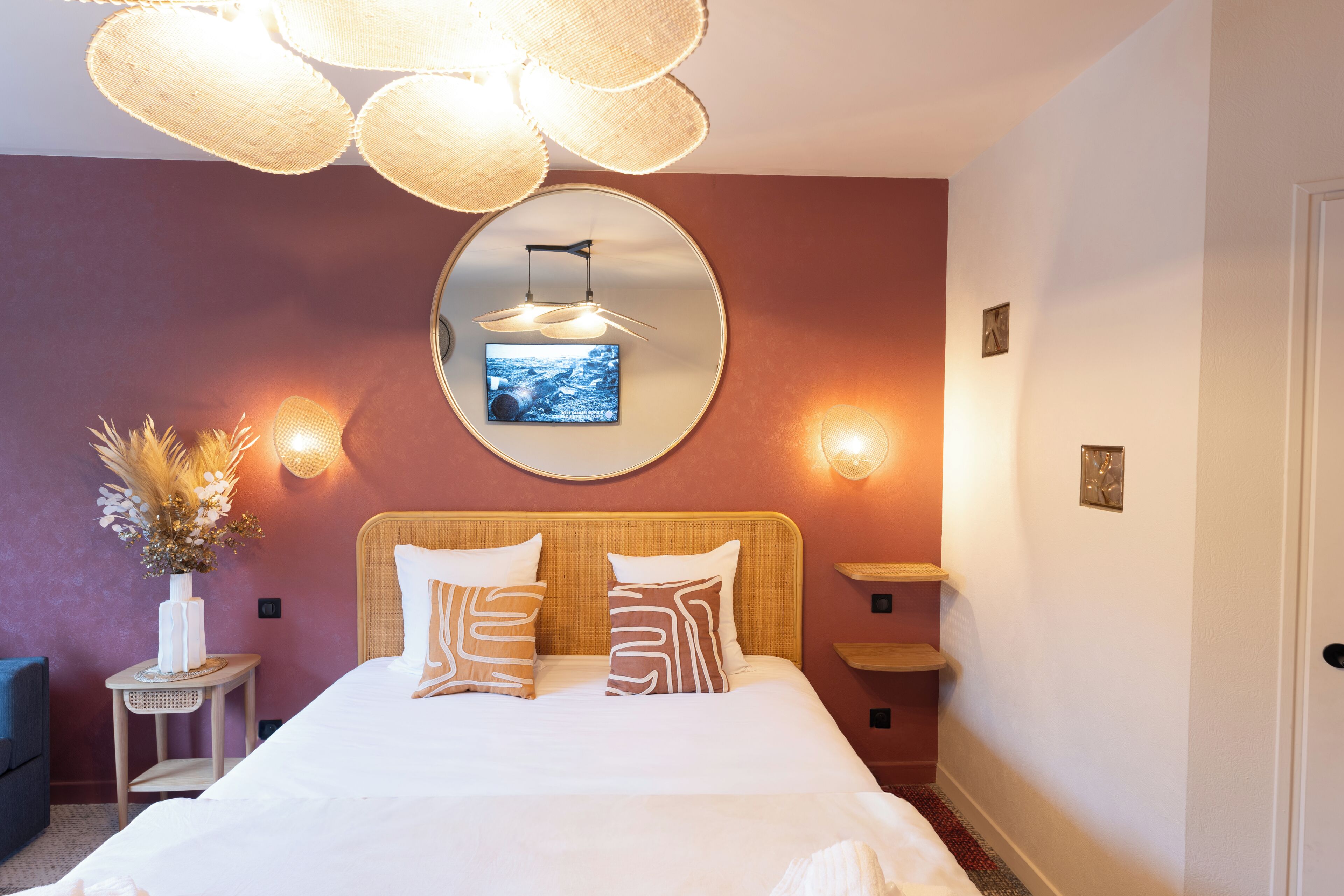 Un dormitorio con cama, mesitas de noche, un espejo, luces empotradas en la pared y un jarrón decorativo.