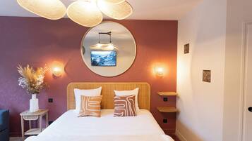 Un dormitorio con cama, mesitas de noche, un espejo, luces empotradas en la pared y un jarrón decorativo.