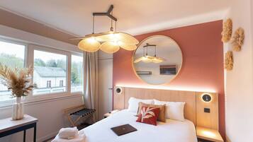 A hotel room with a bed, bedside table, lamp, mirror, and window with a view.