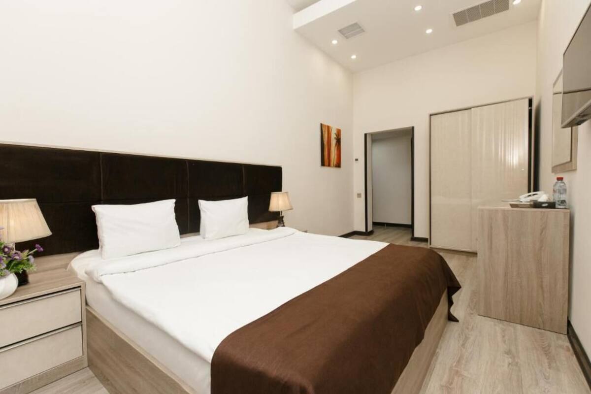 A modern hotel room with a large bed, bedside tables, a wardrobe, and a mirror.