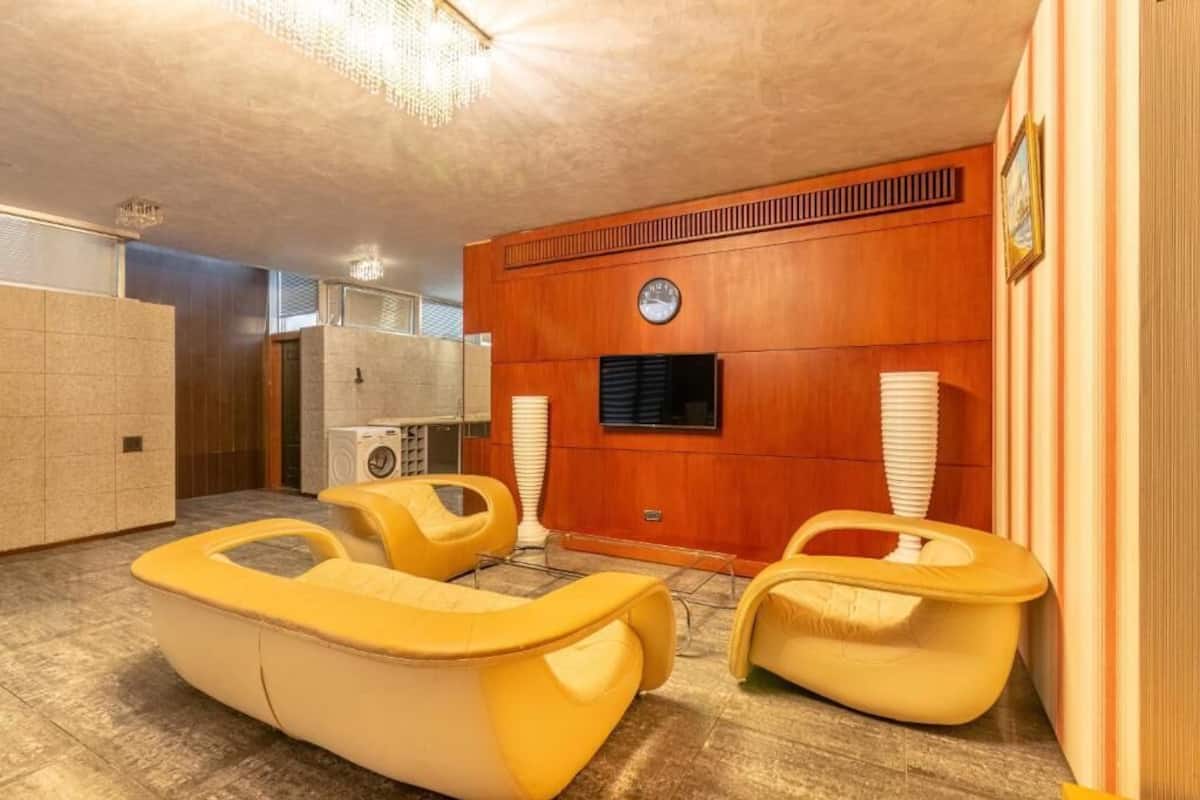 A room with a wooden wall, a clock, and two yellow chairs.