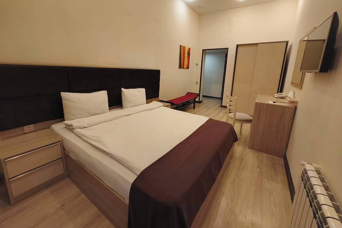 A modern hotel room with a large bed, bedside tables, a desk, and a wardrobe.