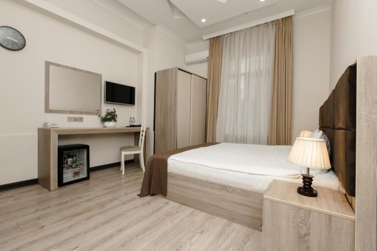A hotel room with a bed, bedside table, desk, chair, and a TV.
